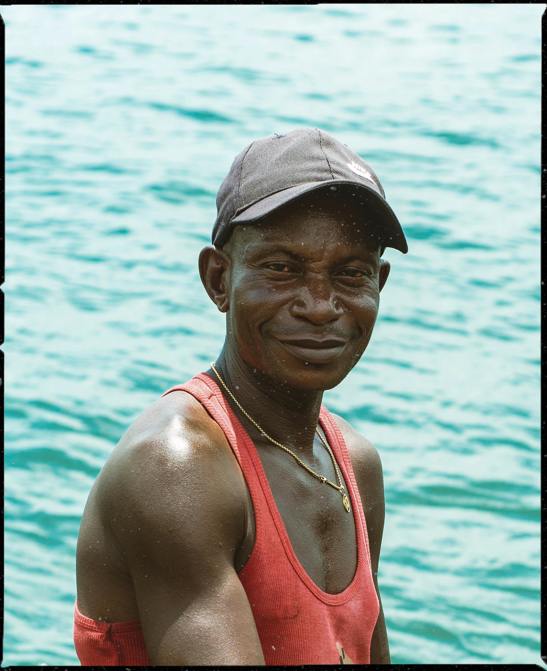 A smiling man in a red tank top enjoying a sunny day by the water.