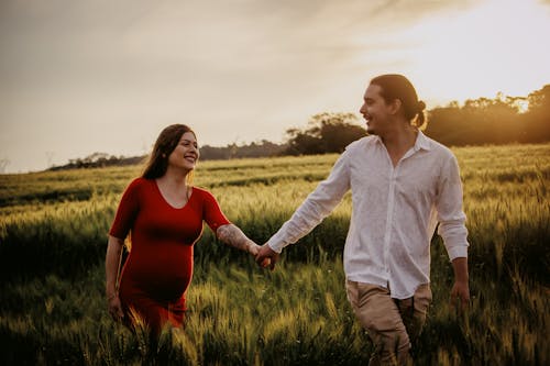 Pregnant Woman and Man Holding Hands While Running on Grass Field 