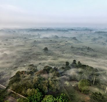 Aerial view of a foggy rural landscape in Banten, Indonesia, showcasing lush greenery and serene morning ambiance. - Fotografer Sidoarjo