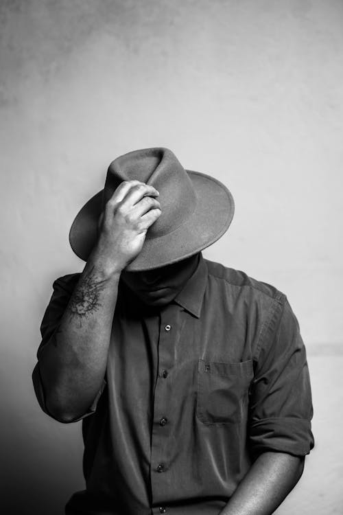 Black and white of unrecognizable young tattooed guy adjusting trendy hat and looking down