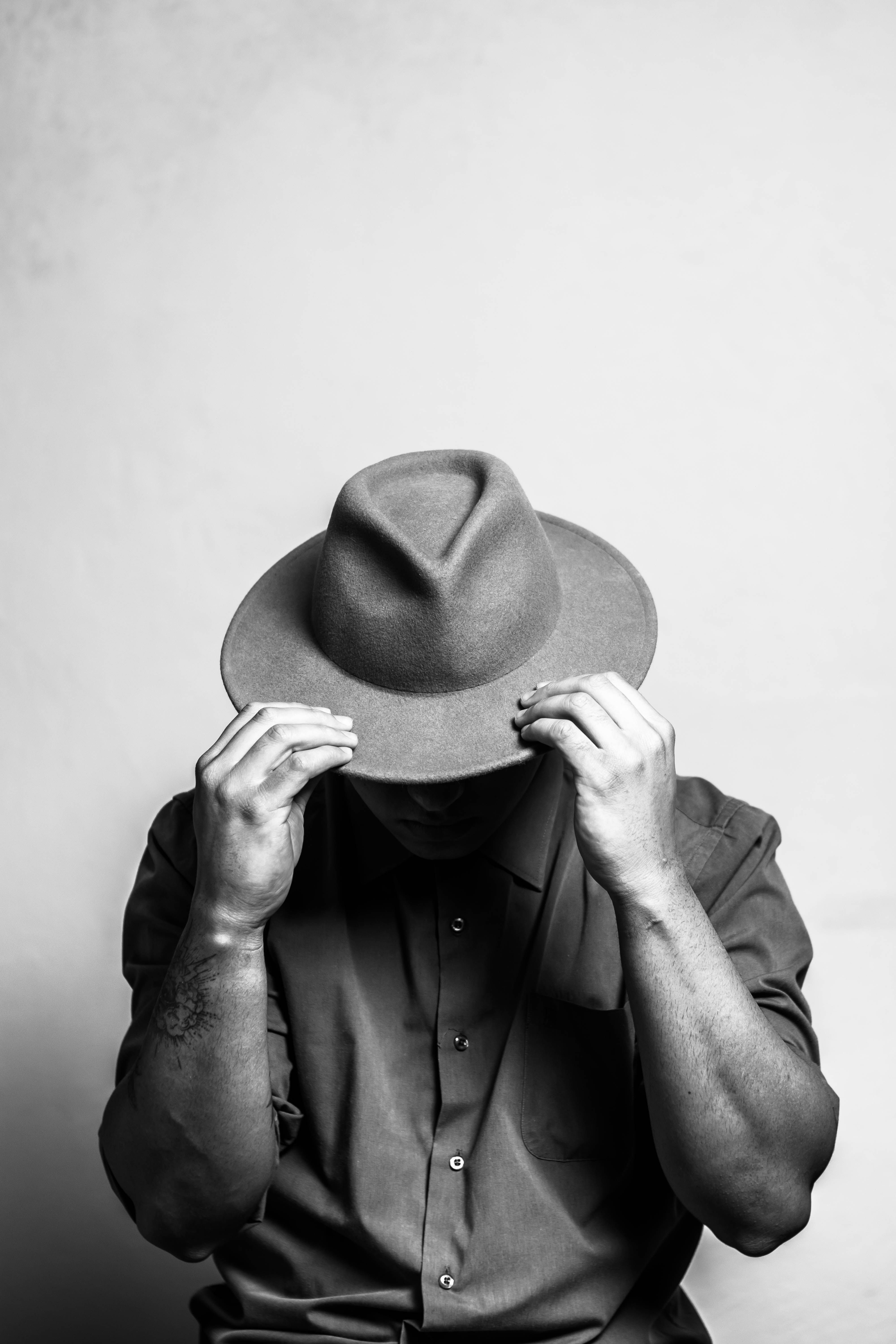 Monochrome portrait of a person adjusting a fedora hat, showcasing style.