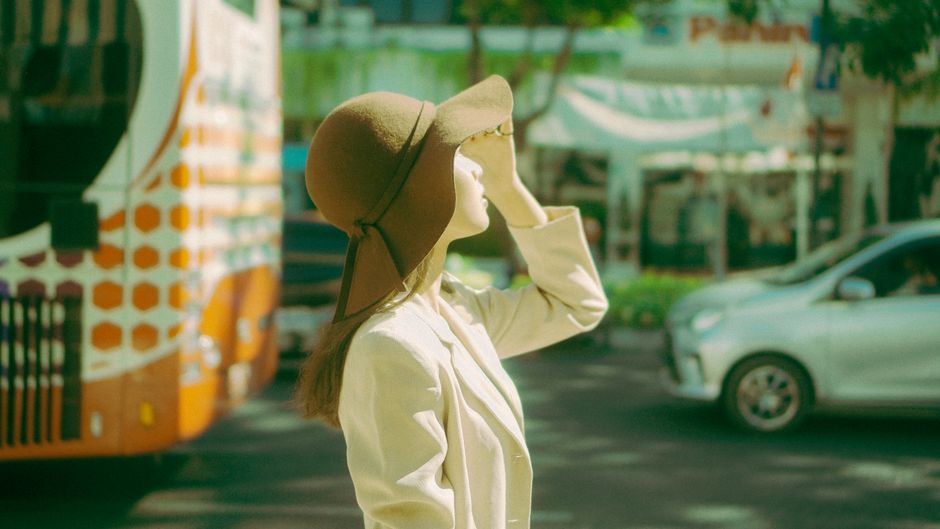 Woman in a beige coat with a hat standing on a city street during the day.