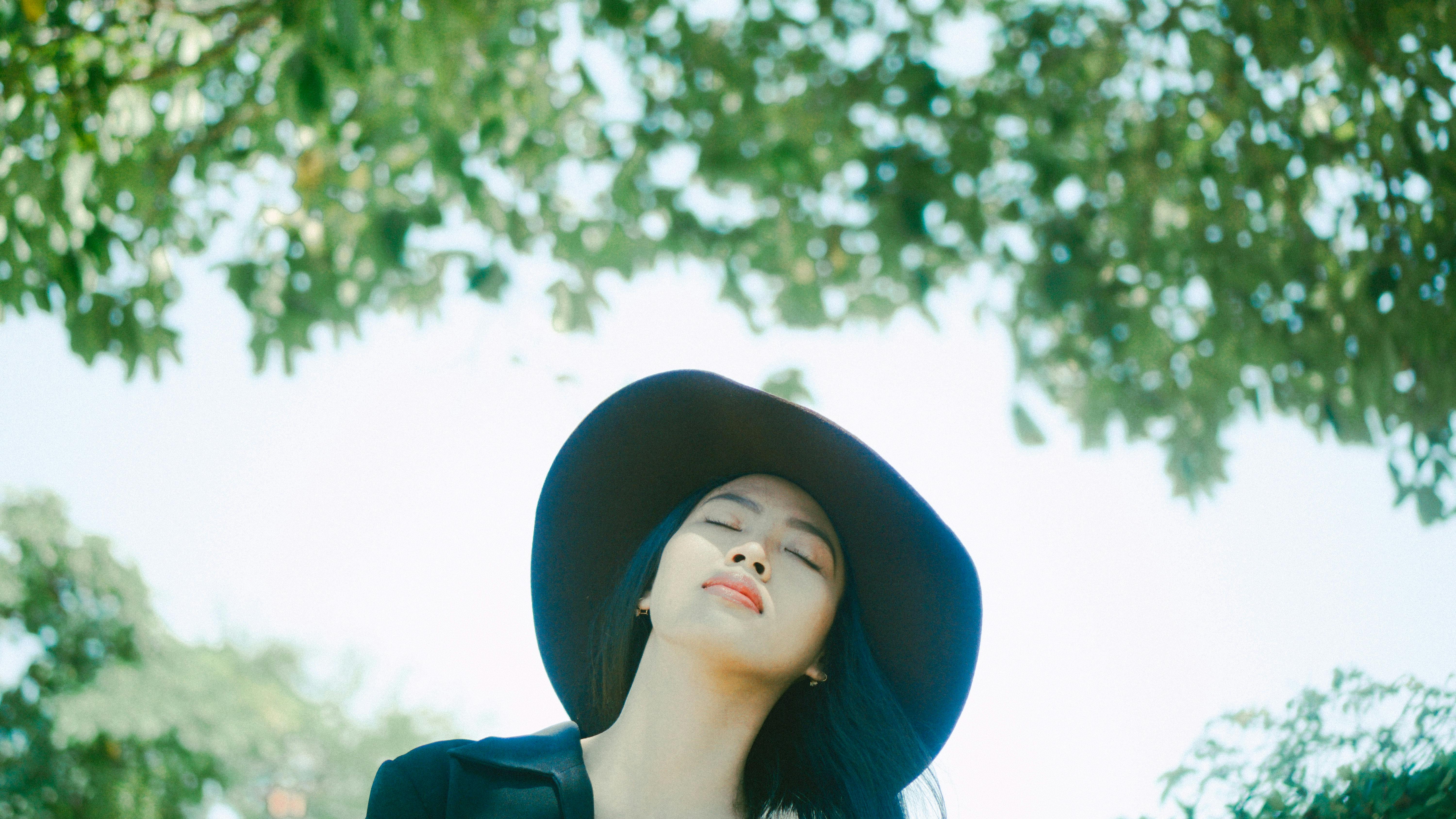 一位亚洲妇女戴着帽子，闭着眼睛，在户外大自然中享受阳光的肖像