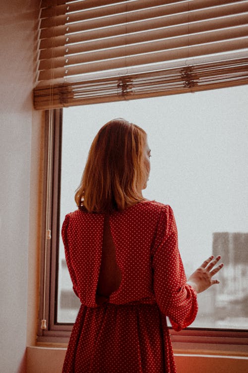 Faceless woman looking out window at home