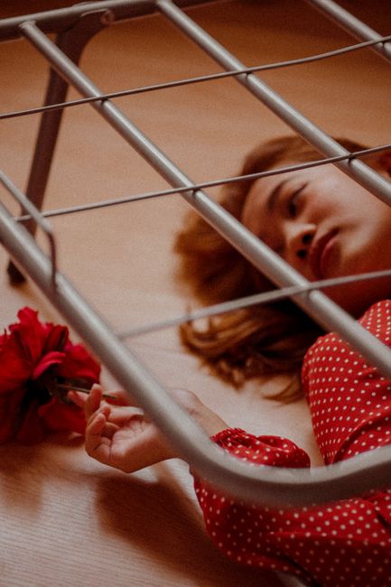 A young woman lies contemplatively on the floor holding a red flower, captured in a warm, intimate setting.