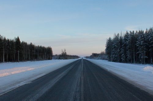 Free Long snow-covered road through a tranquil winter forest, showcasing serene winter beauty. Stock Photo