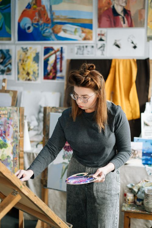 Free A female artist creates a masterpiece in a vibrant studio filled with her colorful artworks. Stock Photo