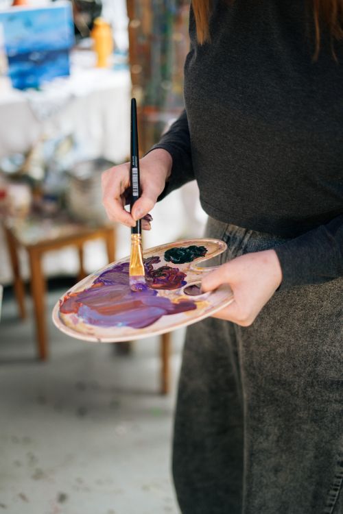 Free Close-up of an artist holding a palette and paintbrush, blending oil paints. Stock Photo