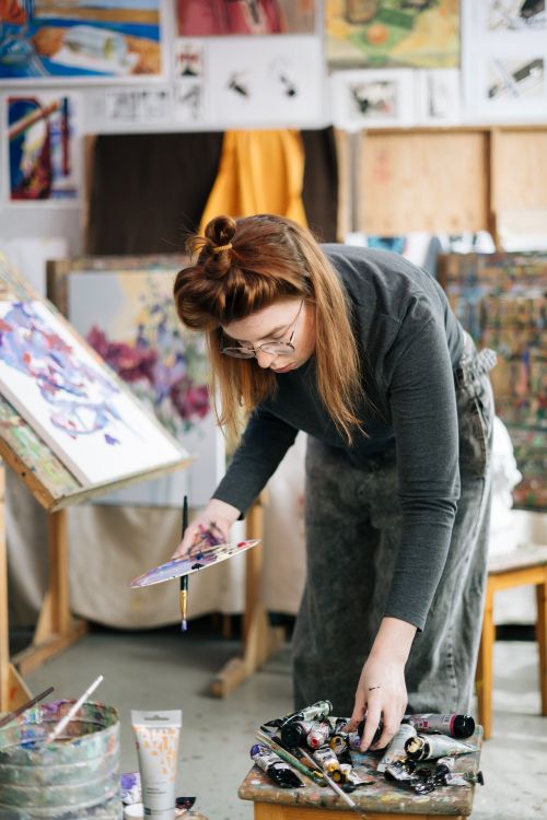 Free Woman artist choosing paint colors in a vibrant workshop setting. Stock Photo
