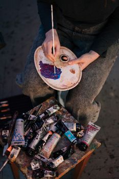 艺术家拿着调色板，用画笔和油漆管混合颜色