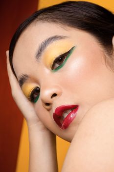 Close-up portrait of a woman showcasing colorful makeup and striking pose with yellow and green eyeshadow.