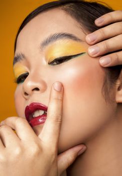 Close-up portrait of a woman with striking yellow eyeshadow and red lips.