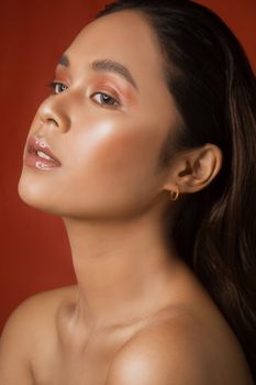 Close-up portrait of a woman with stunning makeup against a vibrant red background.
