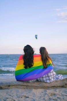 一对夫妇裹着彩虹旗坐在海滩上，拥抱包容与自豪