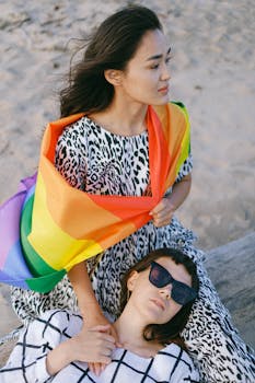 一对快乐的夫妇在海滩上拥抱，展示爱与包容的骄傲旗帜