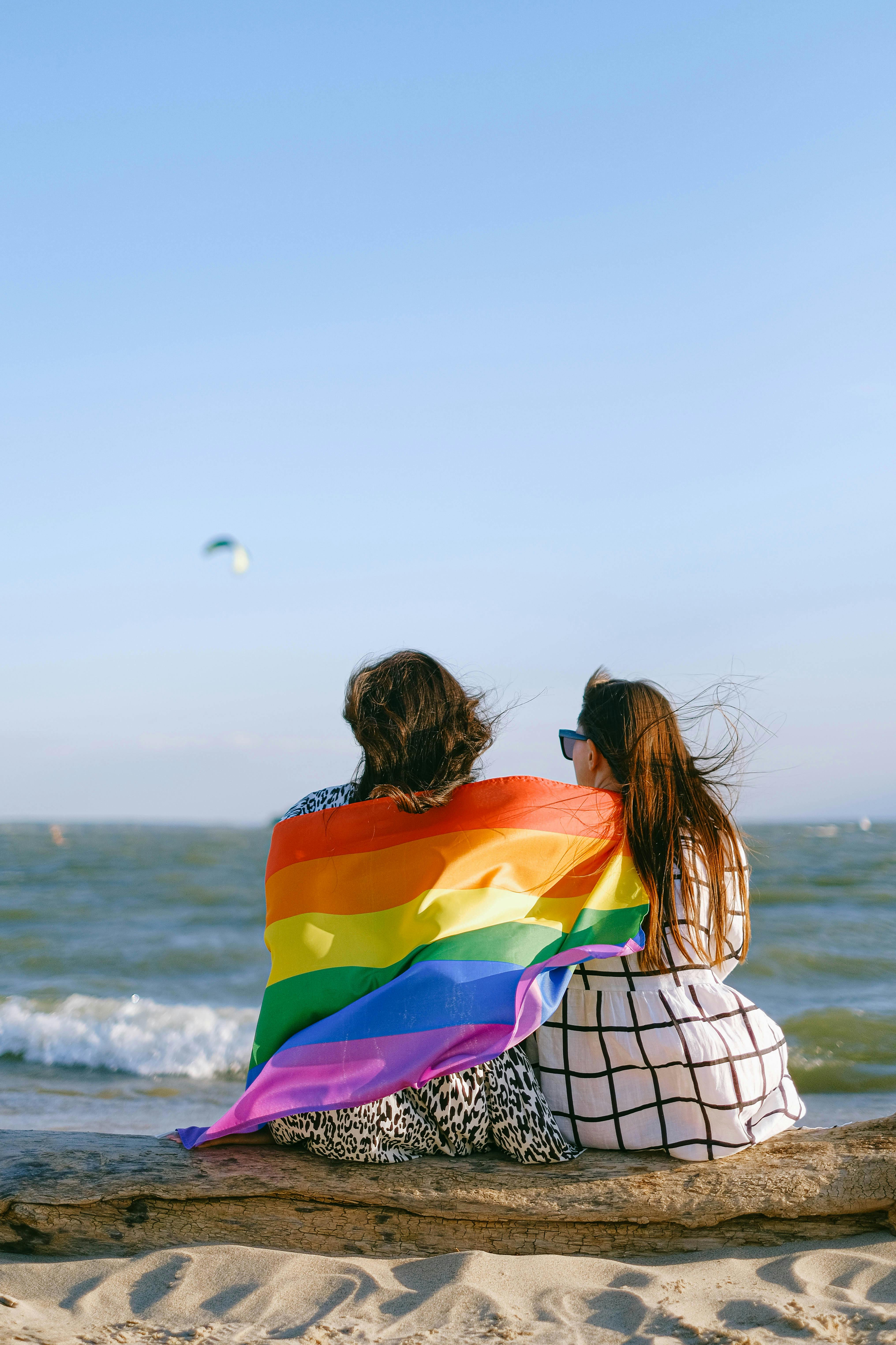 Couple sitting together on a beach with a rainbow flag, symbolizing LGBTQ pride and love.