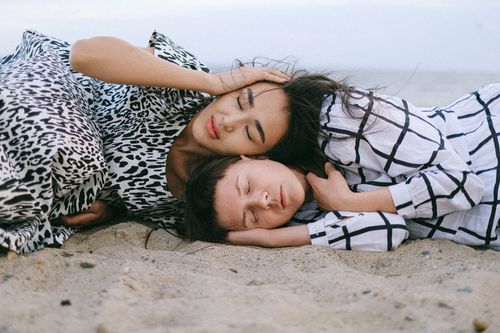 Free Two women sharing a serene moment lying on the sandy beach, capturing tranquility and togetherness. Stock Photo