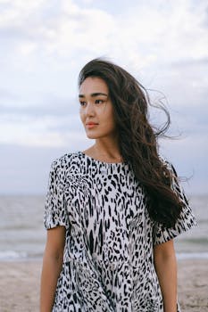 一个穿着时髦动物印花连衣裙的亚洲女人，在大风天站在海滩上