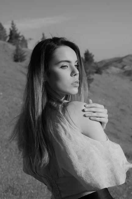 Black and white of pensive thoughtful female with bare shoulder looking away on blurred background of valley