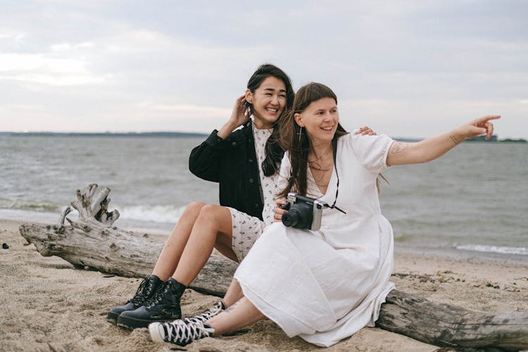 A Couple Sitting On A Log By The Beach