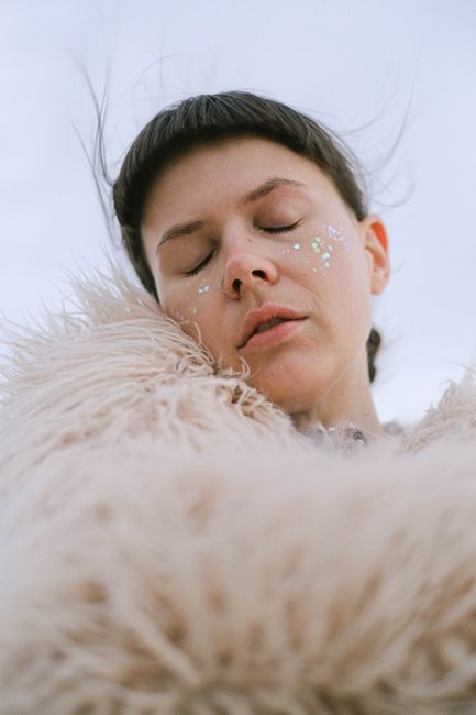 From below view of female in fur coat with closed eyes and spangle on cheeks