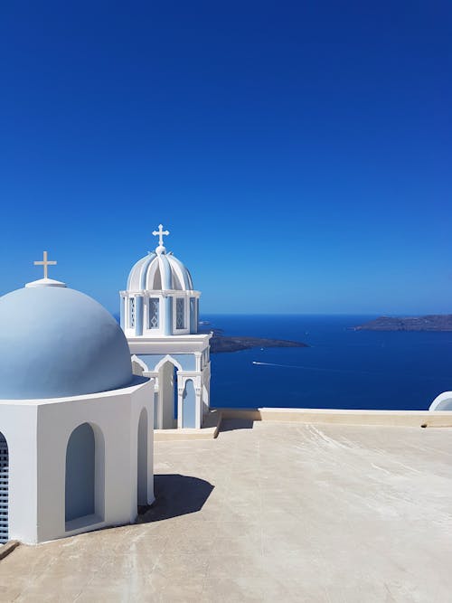 White and blue cathedrals with crosses and domes on shore of vast ocean under blue wide sky