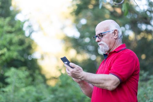 Free Elderly man checking his phone in a sunny park. Stock Photo