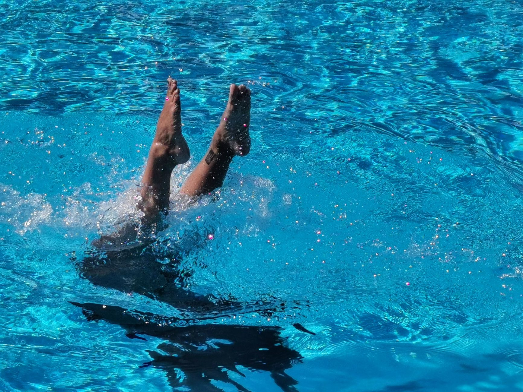 Dynamic scene of legs diving into a bright blue pool, creating a refreshing splash.