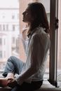 一位身穿白衬衫、老练的年轻人在窗边摆姿势，拥抱自然光