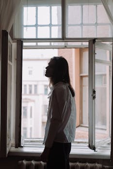 Silhouette of a man standing by an open window in an apartment, creating a cinematic ambiance.