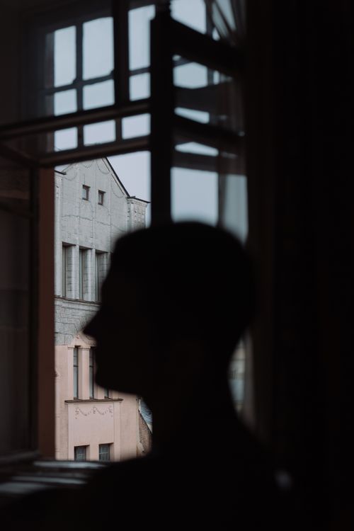 Free A silhouette of a person in front of an open window overlooking buildings. Stock Photo