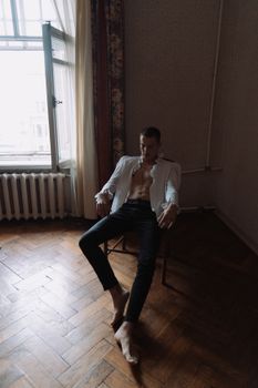一个男人穿着未系扣的衬衫，时髦地坐在昏暗的房间里