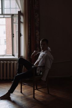 一个穿着白衬衫的男人沉思着坐在窗边，室内弥漫着一种戏剧性的、喜怒无常的气氛