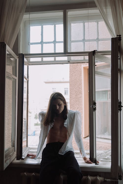 Free Woman in White Long Sleeve Shirt Standing Near Glass Window Stock Photo