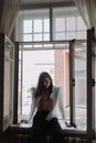 Woman in White Long Sleeve Shirt Standing Near Glass Window