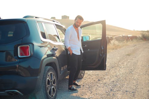 Man in White Long Sleeves and Black Pants Standing Beside a Car 