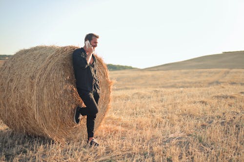 Man Leaning against Hay Bale and Talking on Smartphone