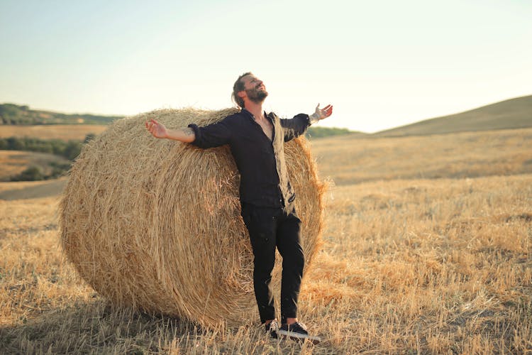 Man Standing By Hay Bale In Field