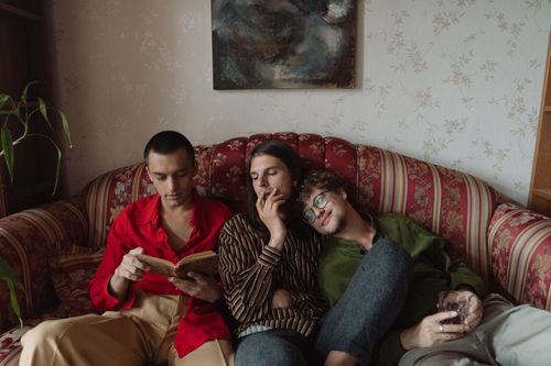 Free Three young men enjoying leisure time indoors, reading and smoking on a cozy sofa. Stock Photo