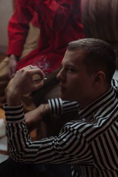 一个穿着条纹衬衫的男人在室内吸烟，营造出阴郁的氛围