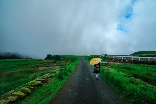 在印度梅加拉亚邦的一条乡村道路上，一个人打着雨伞，天空多云
