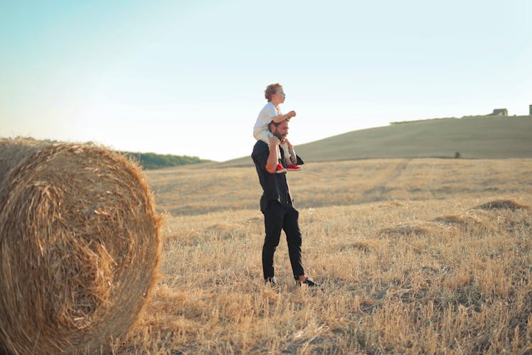 Father Giving His Child Piggyback Ride In Field