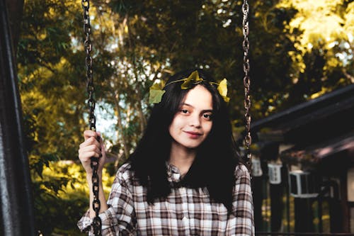 Woman in Plaid Long Sleeves With Green Leaves on Hair Sitting on Swing 