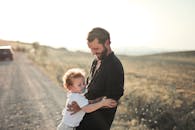 Man in Black Jacket Carrying Baby in White Onesie