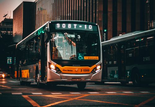 Free Low angle of modern bus riding on asphalt road amidst building of contemporary city at sunset Stock Photo