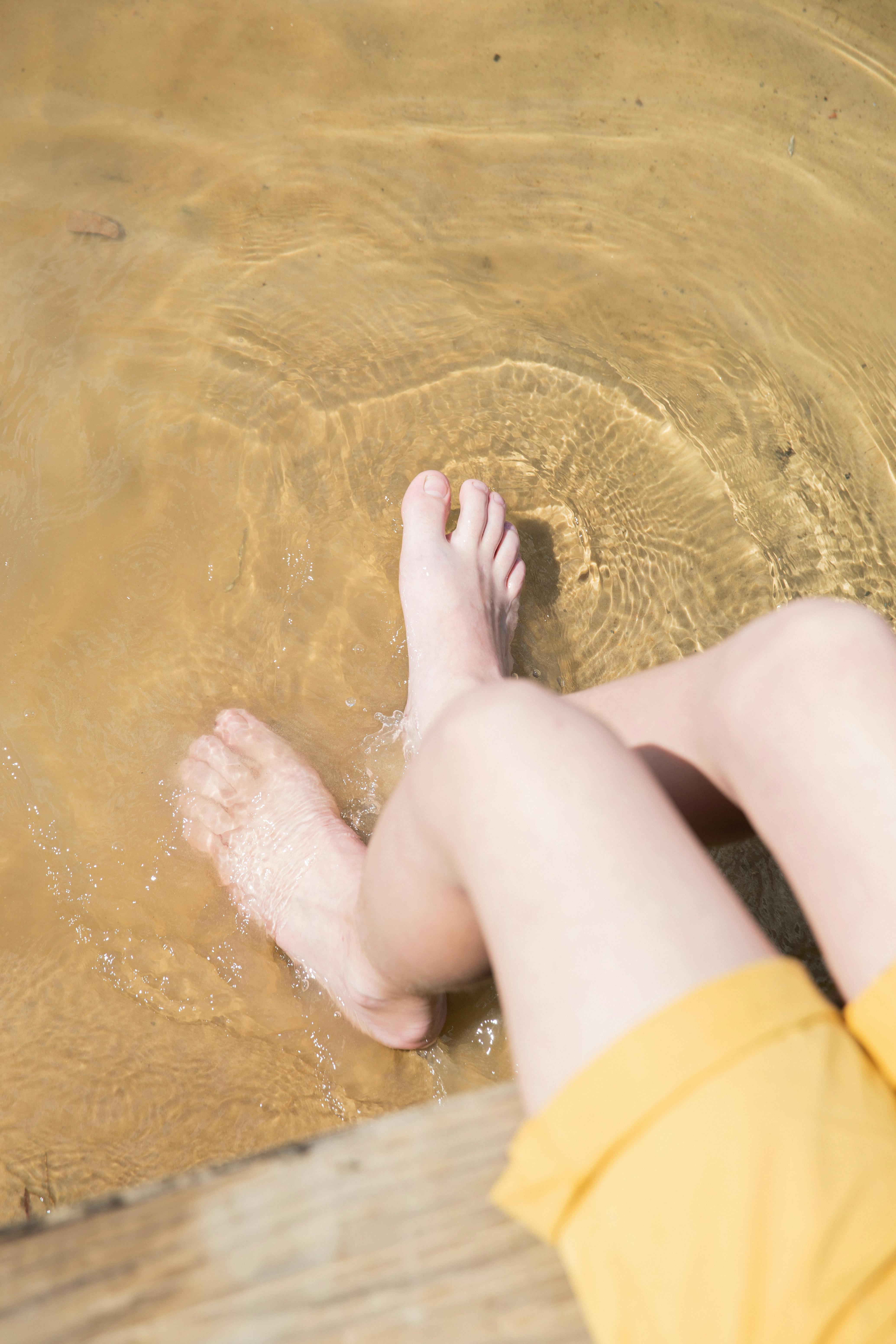 夏日阳光明媚，一个年幼的孩子将脚放在清澈的水中，散发出一种放松的感觉