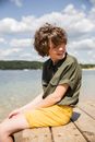 Man in Green Button Up Shirt Sitting on Brown Concrete Floor Near Body of Water during