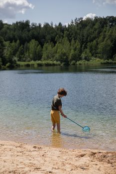 阳光明媚的日子里，一个小男孩用渔网在平静的湖岸边探索