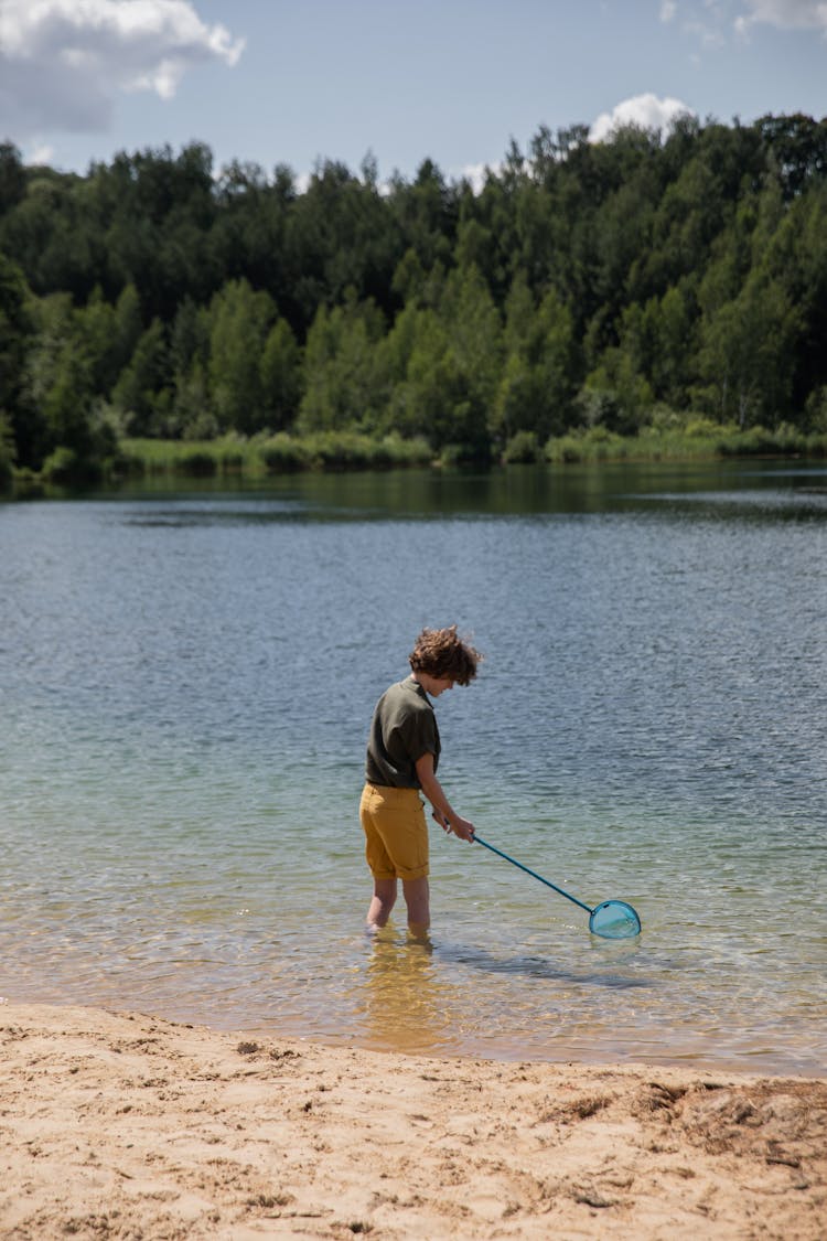 Boy Standing In The Water With A Fishing Net