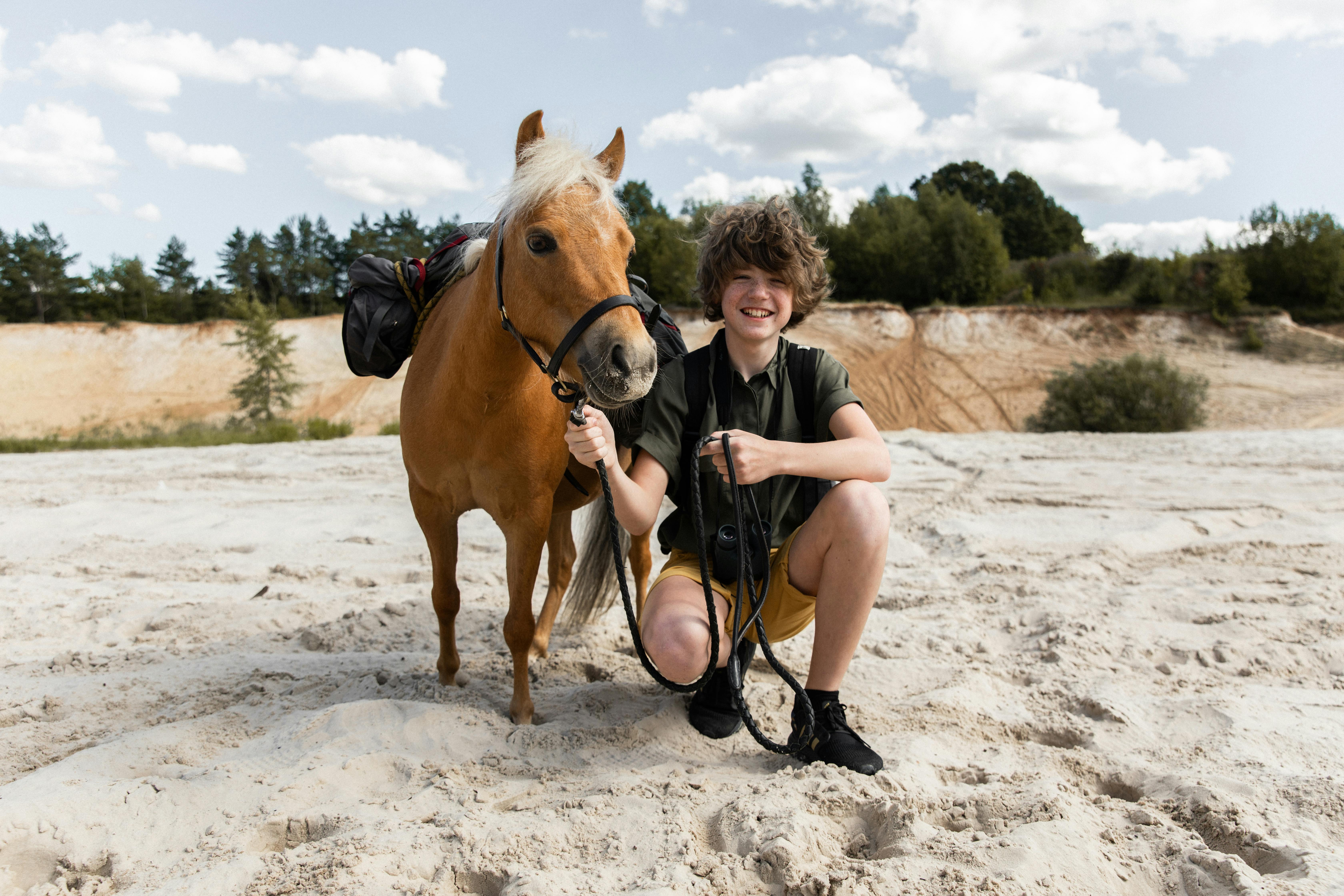 teenage boy crouching next to a pony holding him by the harness